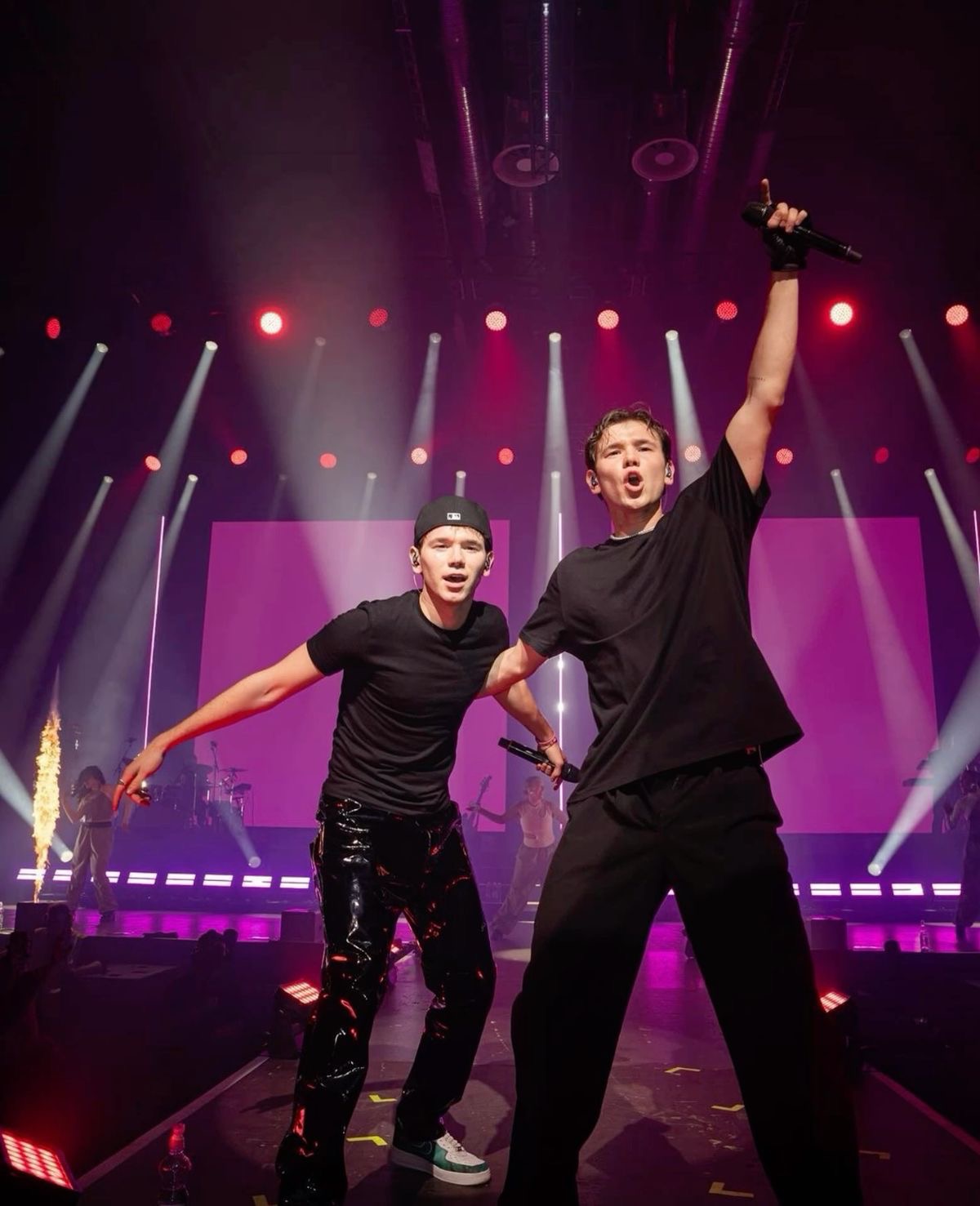 Marcus & Martinus performing with an arm raised as stage flames shoot up