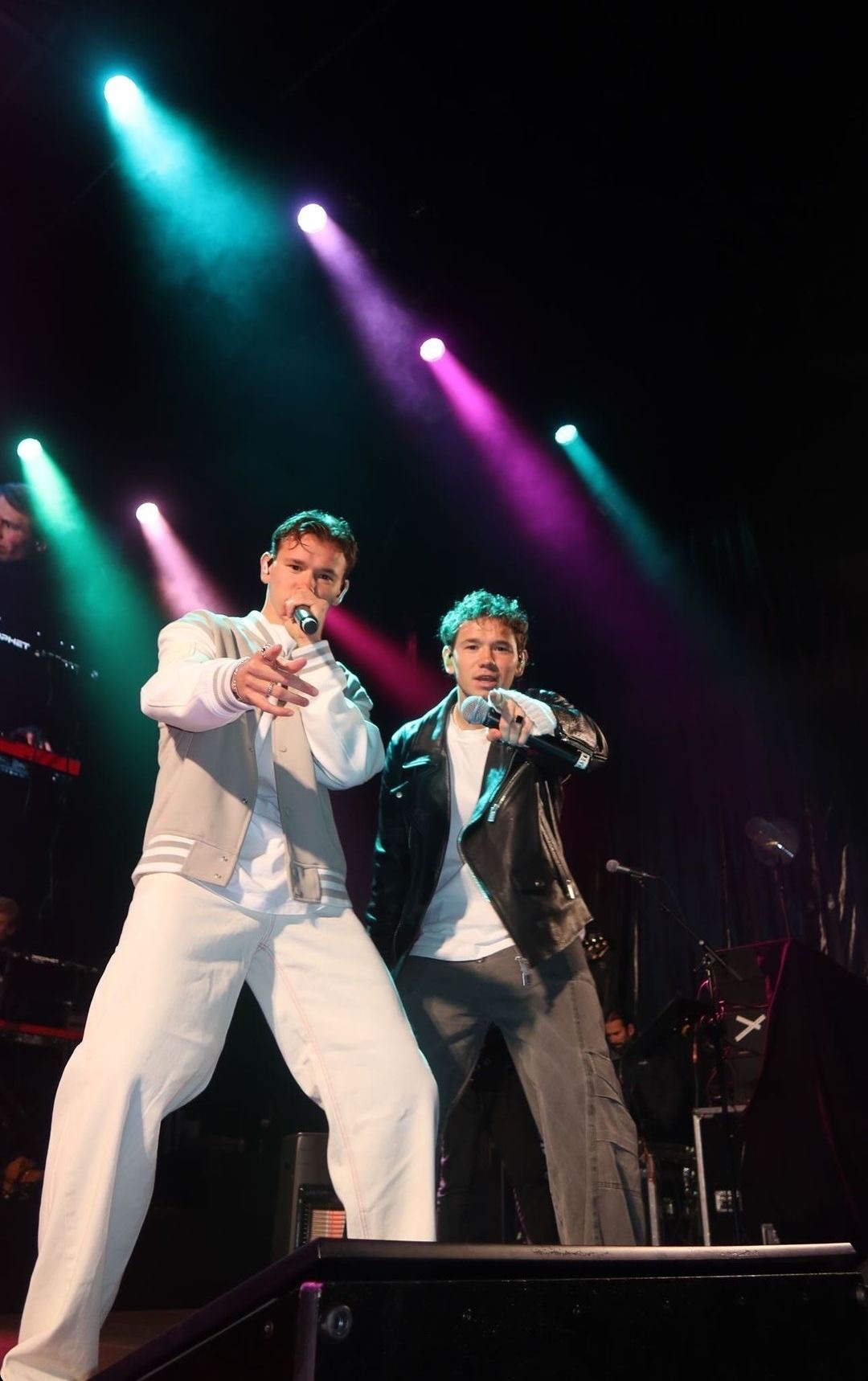 Marcus & Martinus pointing to the crowd on a stage lit with teal and magenta beams
