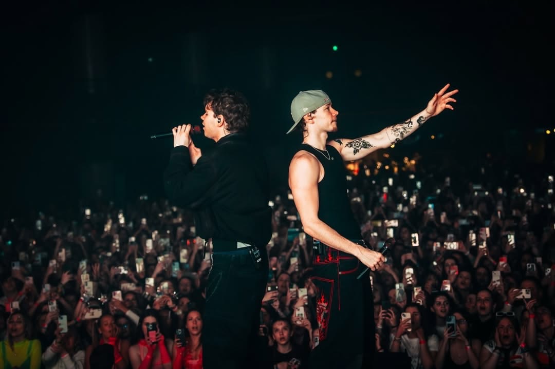 Marcus & Martinus back to back on the runway reaching out to fans, surrounded by a sea of glowing phone screens